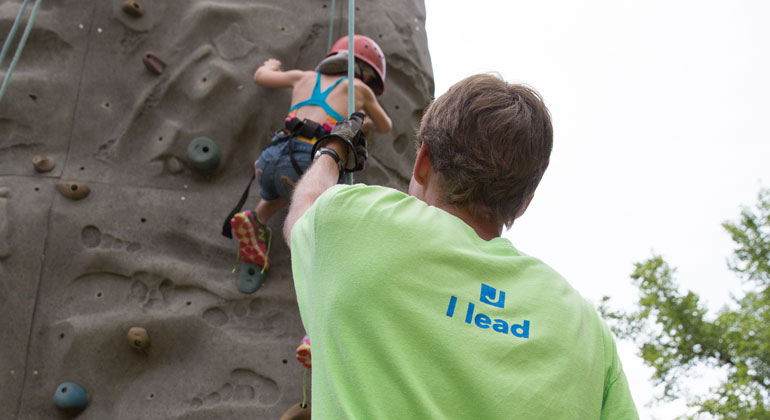 camp counselor belaying camper on rock wall