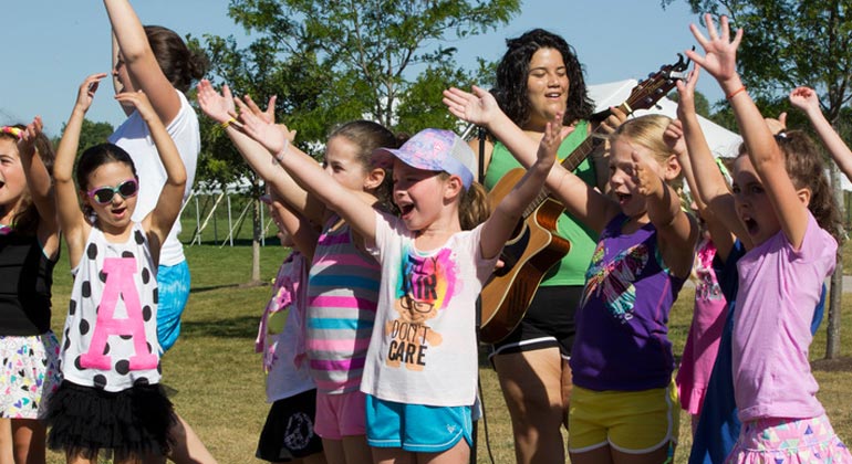 girl campers singing while counselor plays guitar