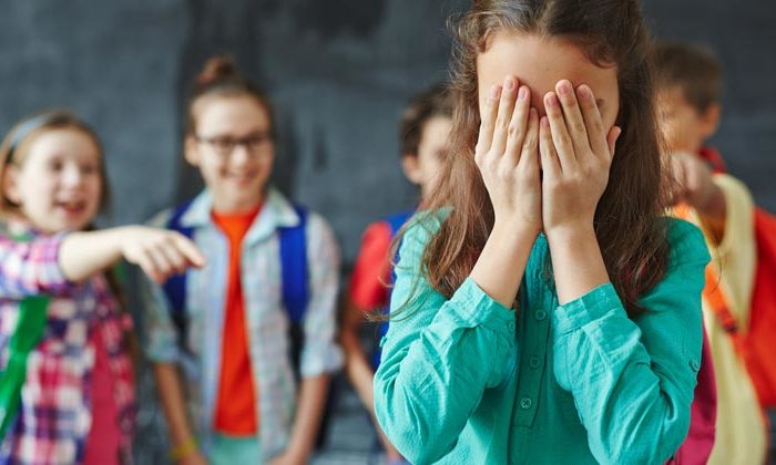 group of kids teasing and pointing at girl covering her face