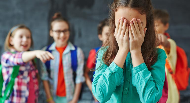 group of kids teasing and pointing at girl covering her face