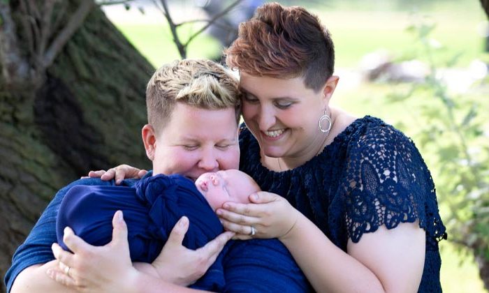 two moms smiling and holding their baby