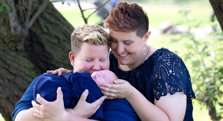 two moms smiling and holding their baby