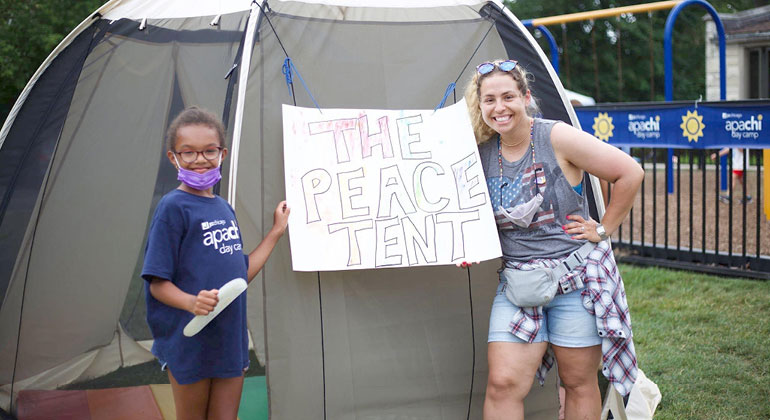 Camper and counselor in front of tent with sign that reads "The Peace Tent"
